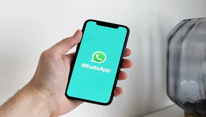 The image shows a person holding a phone that has a WhatsApp logo on it. — Pexels