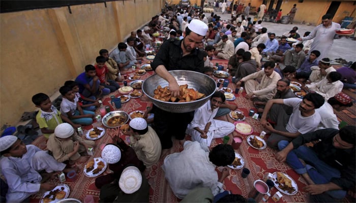 A man distributes samosas, a traditional delicacy consumed during the holy fasting month of Ramadan to men before breaking their fast in Rawalpindi, Pakistan, June 19, 2015. — Reuters